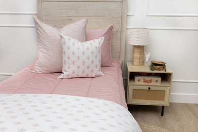 A twin bed made with pink zipper bedding and light pink and floral pillows and blanket.