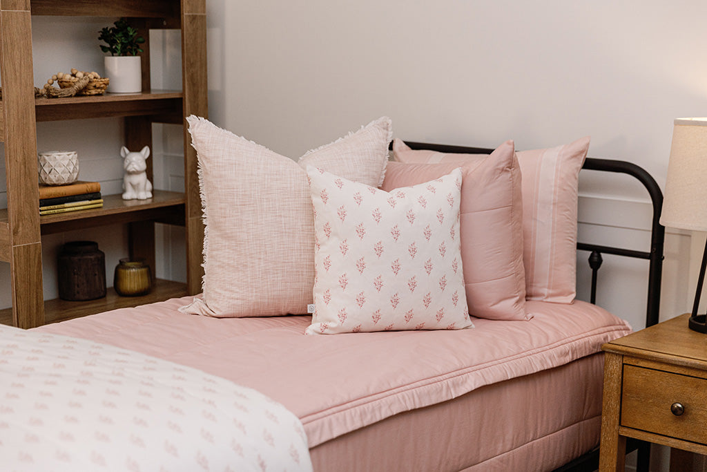 A bed made with pink zipper bedding and an assortment of pink floral and white pillows and blanket.