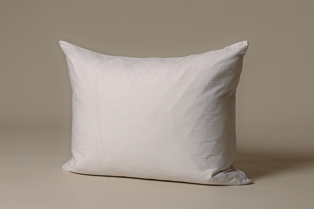 A white and tan crossed pillow on a cream backdrop.
