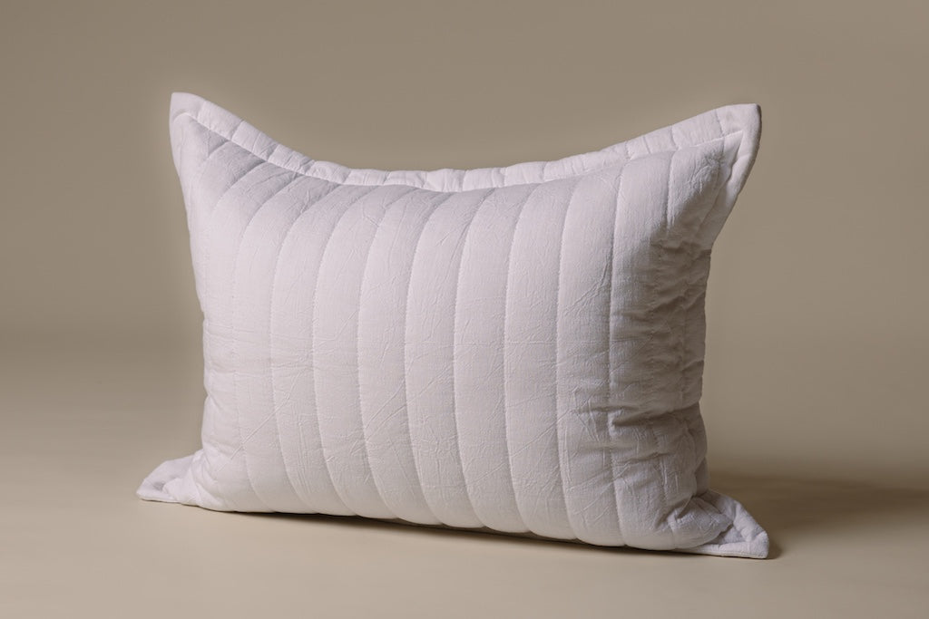 A white striped knitted sham on a cream backdrop.