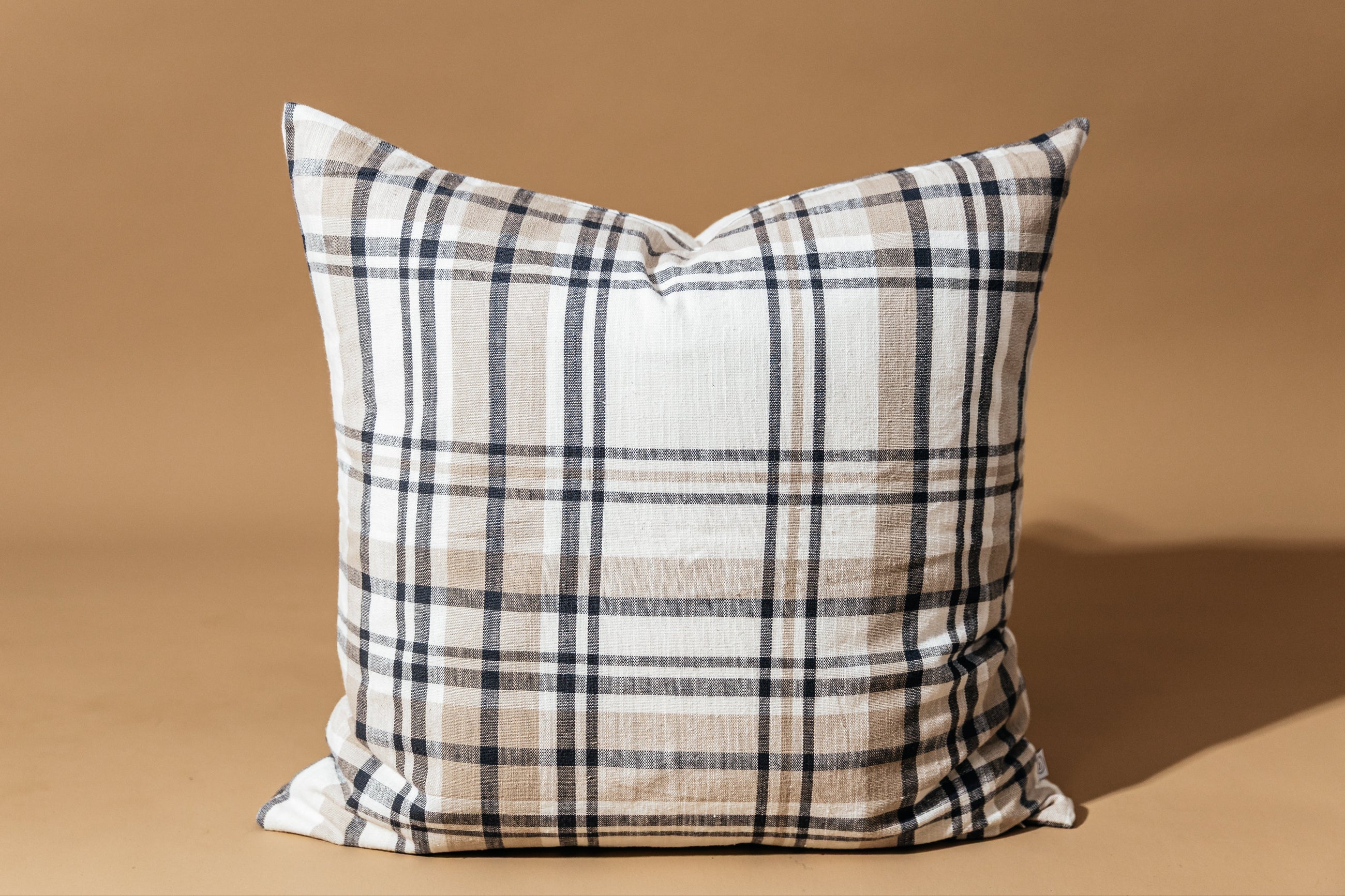 A charcoal, cream, and tan plaid euro pillow on a brown background.