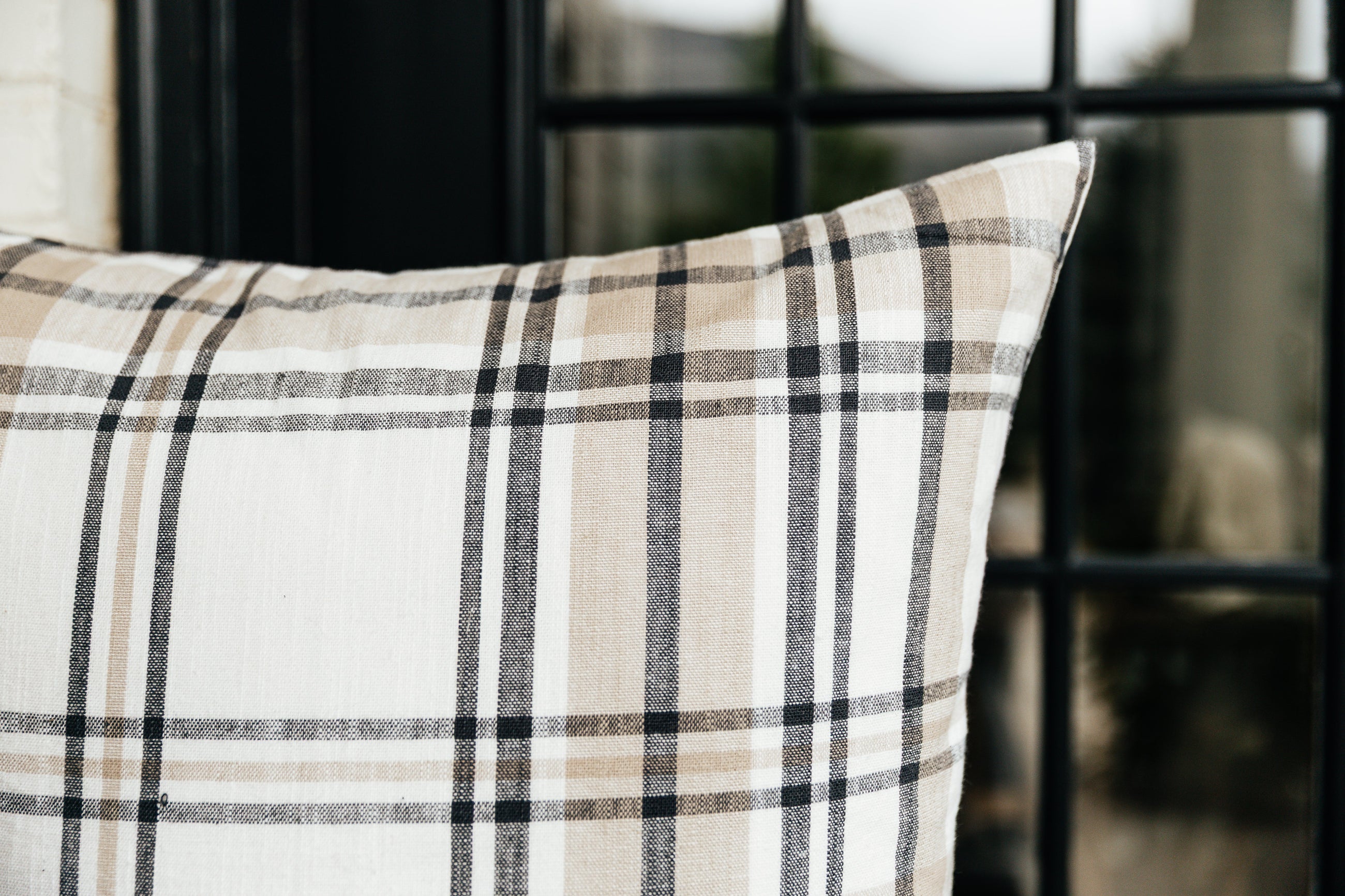 A close up corner view of a charcoal, cream, and tan plaid euro pillow.