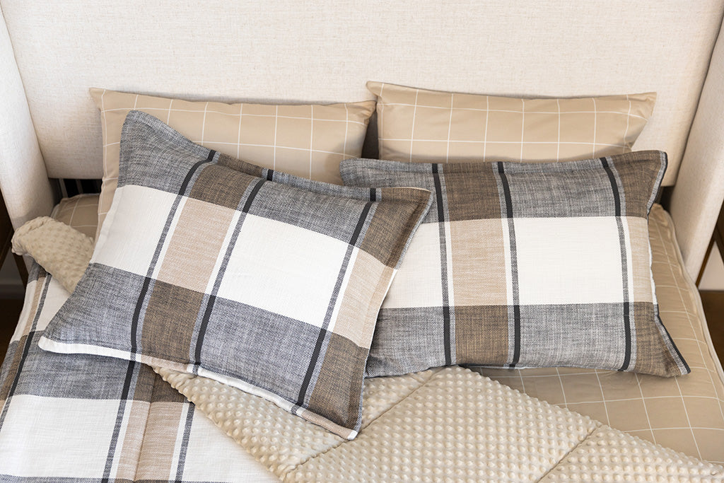 A bed made with cream, charcoal, and tan plaid zipper bedding with the comforter pulled back and pillows on top of the bed.