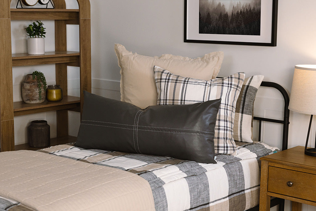 A close up view of a twin bed made with tan, cream, and charcoal zipper bedding and an assortment of neutral pillows and blanket.