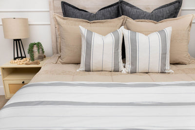 A bed made with tan zipper bedding and an assortment of neutral and striped throw pillows and blanket.