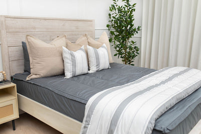 A bed made with gray zipper bedding and an assortment of neutral and striped throw pillows and blanket.