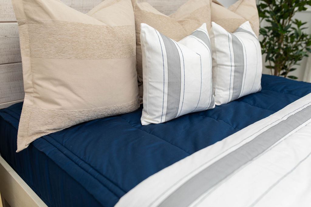A close up view of a bed made with navy blue zipper bedding and an assortment of neutral and striped throw pillows and blanket.