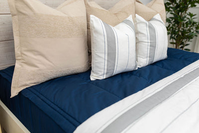 A close up view of a bed made with navy blue zipper bedding and an assortment of neutral and striped throw pillows and blanket.
