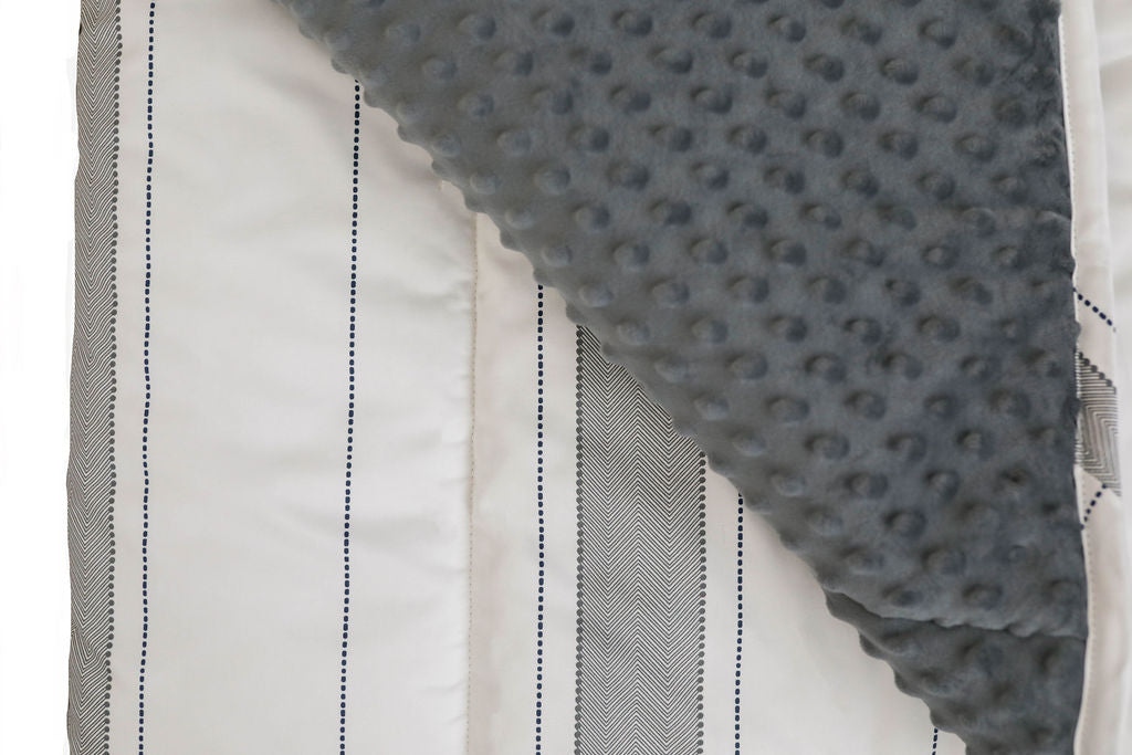 A close up view of a white and gray striped blanket folded over to reveal a soft gray minky interior.