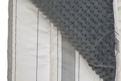 A close up view of a white and gray striped blanket folded over to reveal a soft gray minky interior.