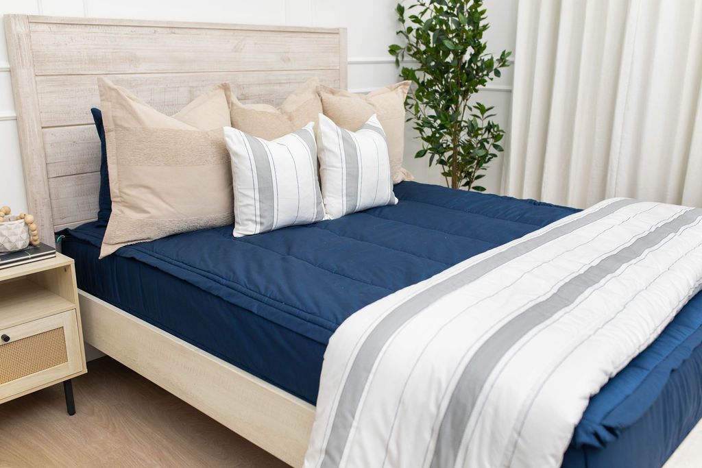 A bed made with navy blue zipper bedding and an assortment of neutral and striped throw pillows and blanket.