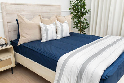 A bed made with navy blue zipper bedding and an assortment of neutral and striped throw pillows and blanket.