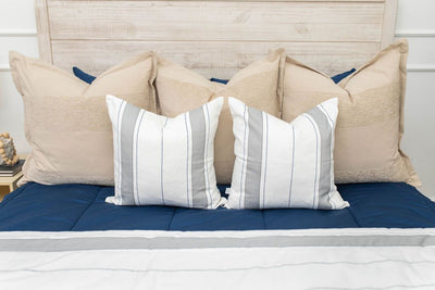 A close up view of a bed made with navy blue zipper bedding and an assortment of neutral and striped throw pillows and blanket.