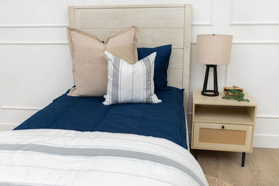 A close up view of a twin bed made with navy blue zipper bedding and neutral and gray striped pillows and blanket.