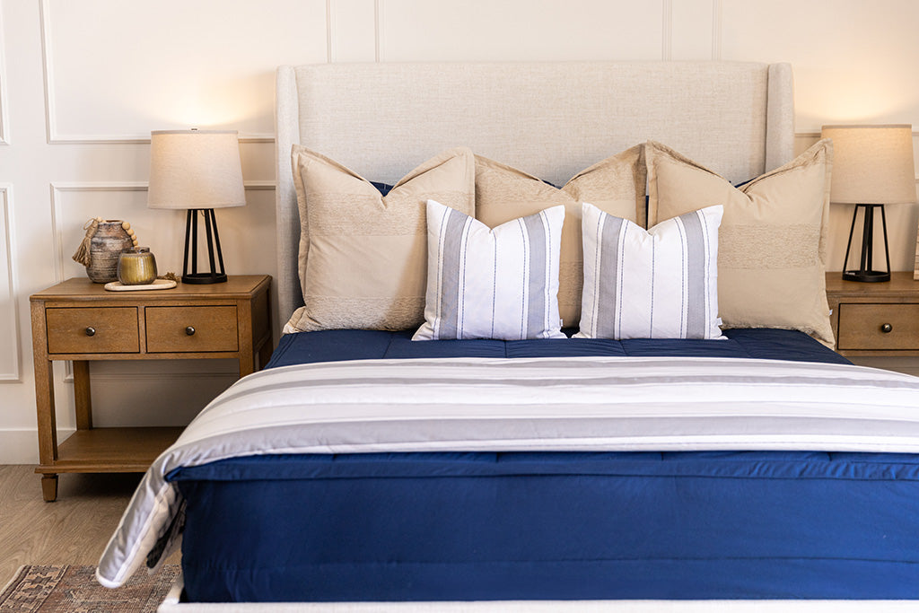 A close up view of a bed made with navy blue zipper bedding and an assortment of neutral and striped throw pillows and blanket.