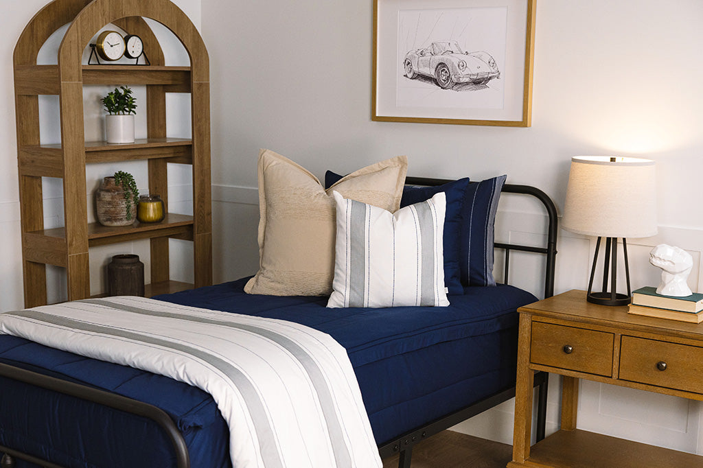 A close up view of a twin bed made with navy blue zipper bedding and neutral striped pillows and blanket.