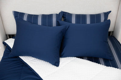 A bed made with navy blue zipper bedding with the comforter pulled back and pillows on top of the bed.