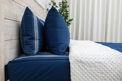 A side view of a bed made with navy blue zipper bedding with the top unzipped halfway down the bed and the comforter folded down.