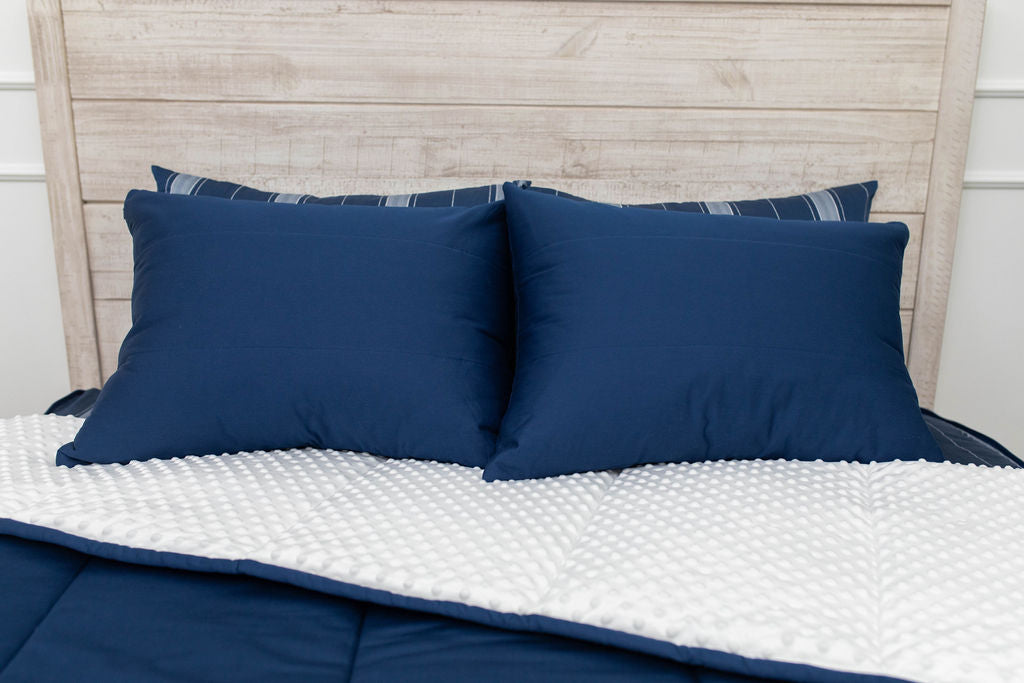 A bed made with navy blue zipper bedding with the comforter pulled back and pillows on top of the bed.