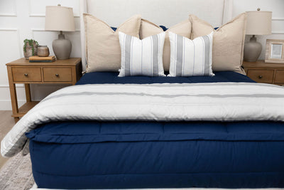 A bed made with navy blue zipper bedding and an assortment of neutral and striped throw pillows and blanket.