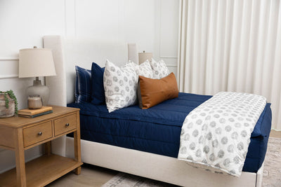 A bed made with navy blue zipper bedding and gray and white pattern pillows and blanket.