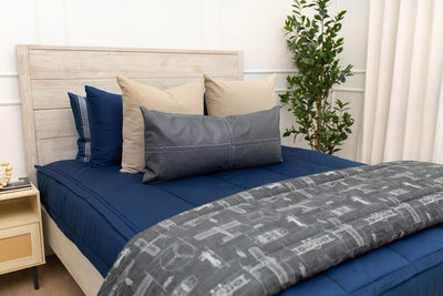 A bed made with navy blue zipper bedding and neutral and dark gray pillows and an airplane pattern blanket.