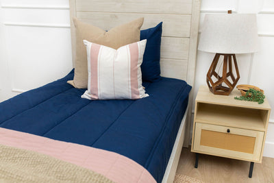 A close up view of a twin bed made with navy blue zipper bedding and neutral pink striped pillows and blankets.