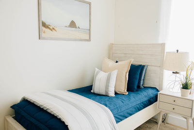 A twin bed made with navy blue zipper bedding and neutral and gray striped pillows and blanket.