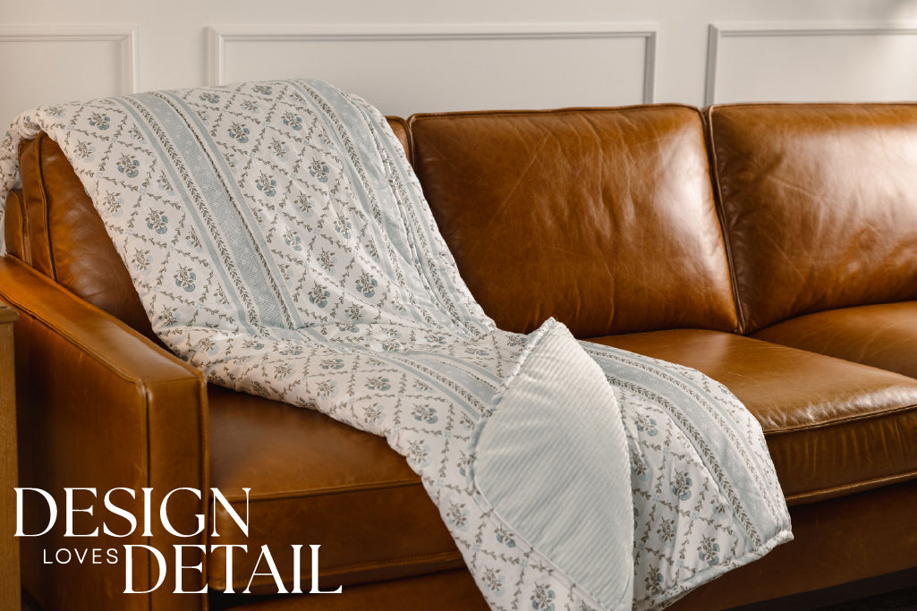 A blue floral and light blue corduroy blanket on an orange leather couch.