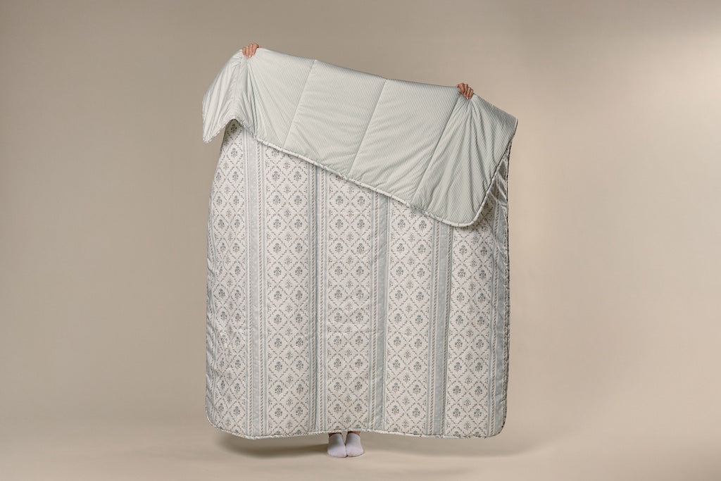 A model holding a blue floral and light blue corduroy blanket on a cream backdrop.