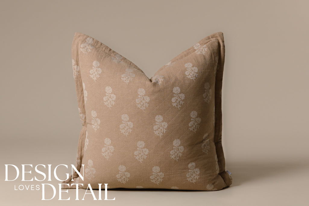 A tan and white floral pillow on a cream background.