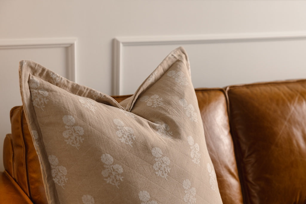 A tan and white floral pillow on an orange leather couch.