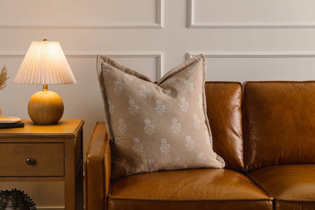 A tan and white floral pillow on an orange leather couch.
