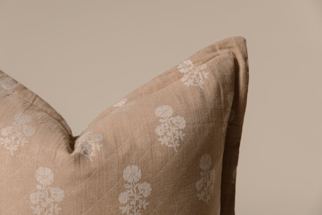 A tan and white floral pillow on a cream background.