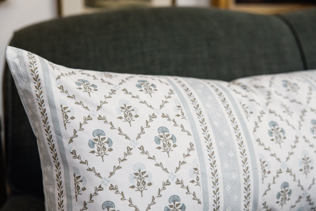 A blue floral lumbar pillow on a blue couch.