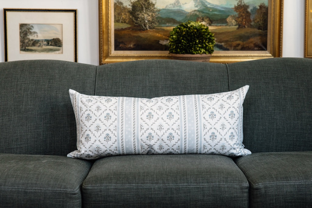 A blue floral lumbar pillow on a blue couch.