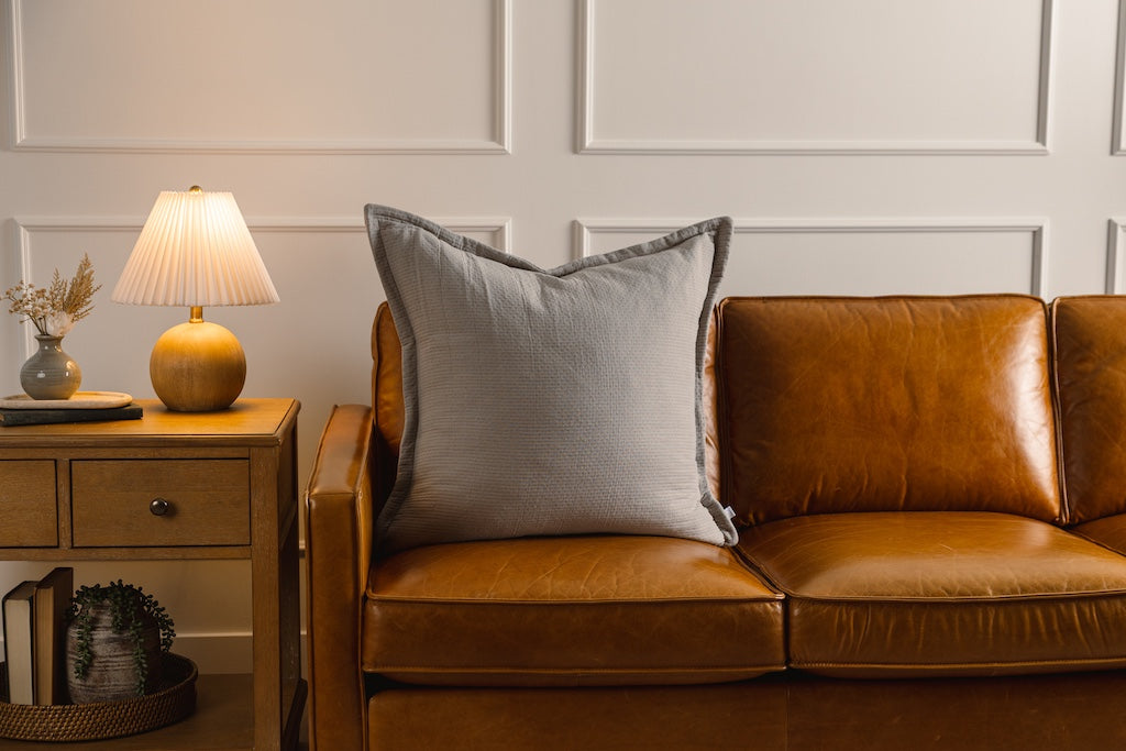 A gray stitched XL pillow on an orange couch.