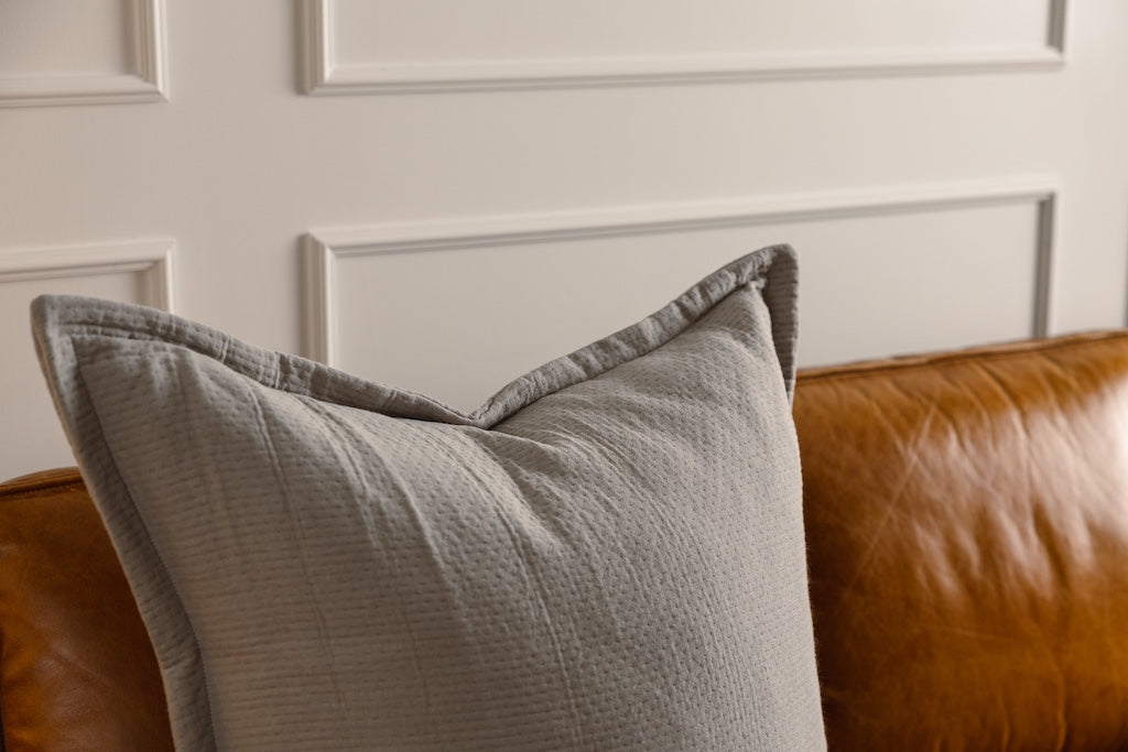 A gray stitched XL pillow on an orange couch.