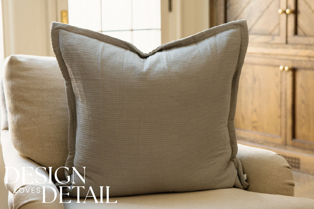 A gray stitched XL pillow on a cream couch.