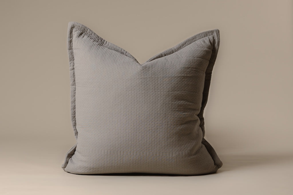A gray stitched pillow on a cream background.