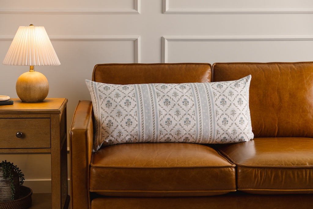 A blue floral lumbar pillow on an orange leather couch.
