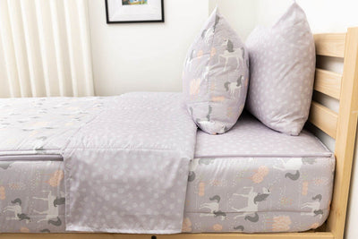 A side shot of a twin bed made with purple unicorn kids zipper bedding, the top unzipped and pulled back slightly and two pillows at the head of the bed