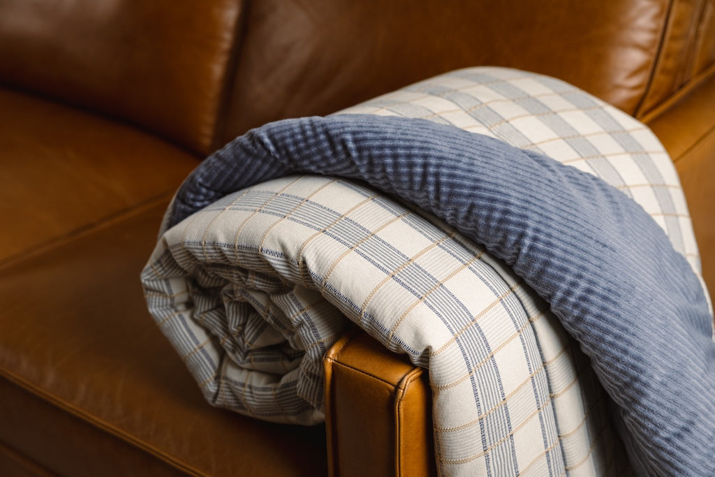 A blue and yellow plaid stitched blanket with a blue corduroy interior on an orange leather couch.