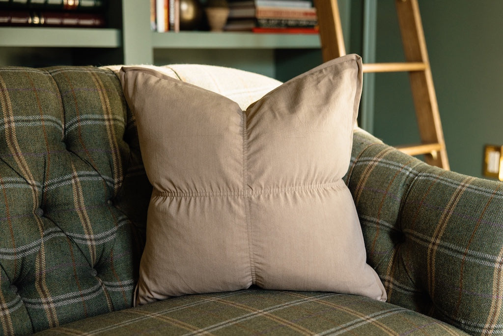 A light brown pillow on a green and plaid sofa.