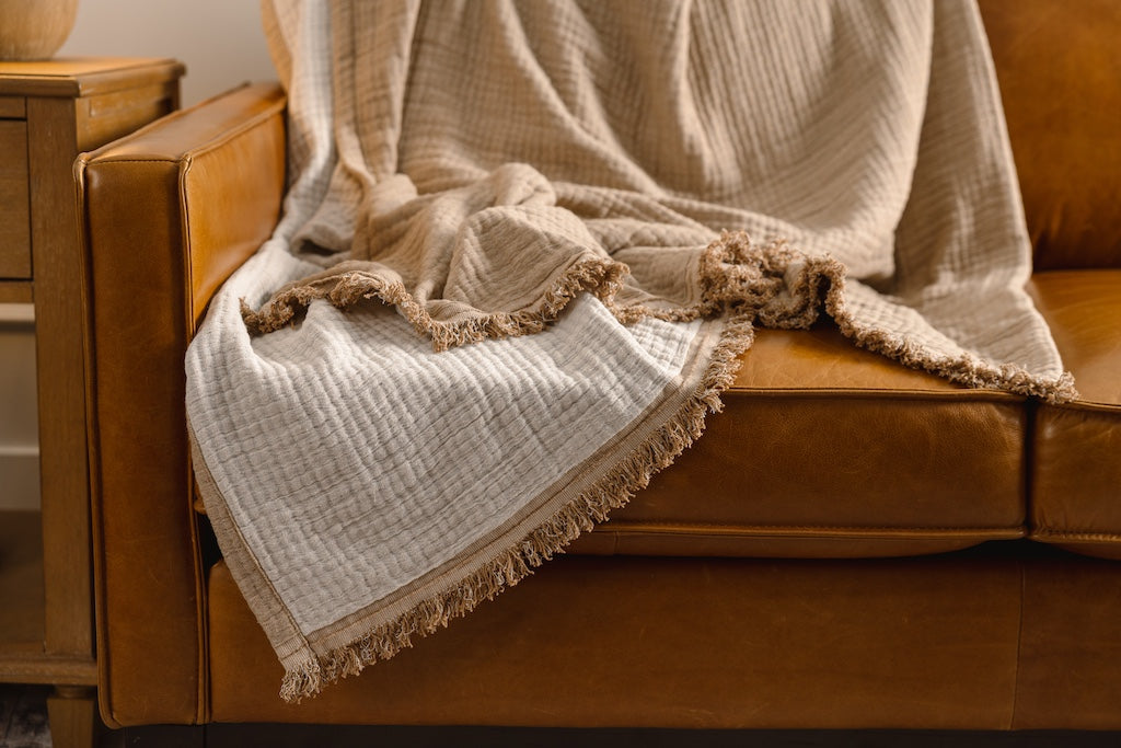 A light brown and cream with a fringed edge throw on an orange leather couch.