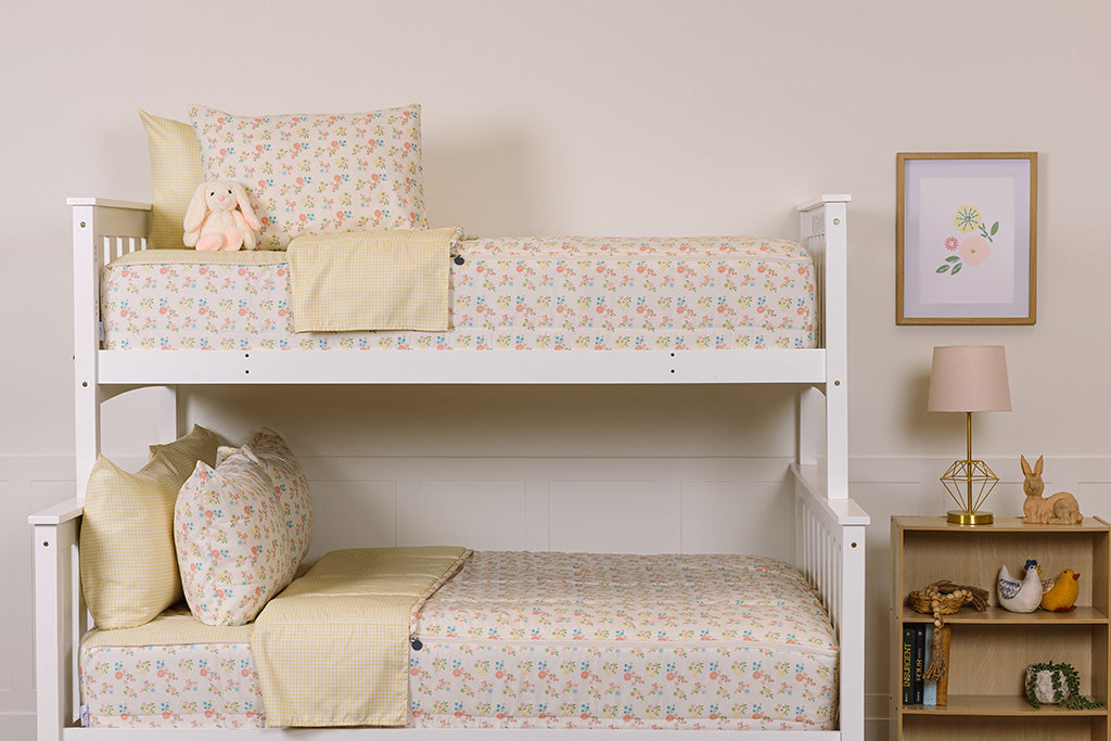 A bunk bed with the top twin and bottom full made with flower and yellow gingham printed zipper bedding and stuffed animals on each bed. 