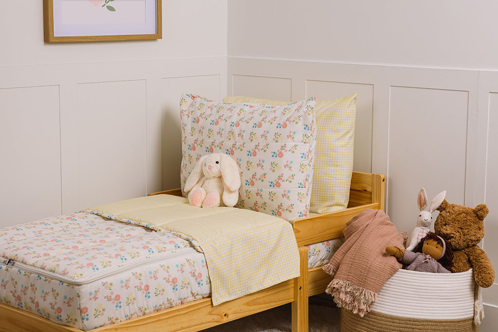 A wooden toddler bed made with flower and yellow gingham printed zipper bedding and a stuffed animal leaning against the pillows.