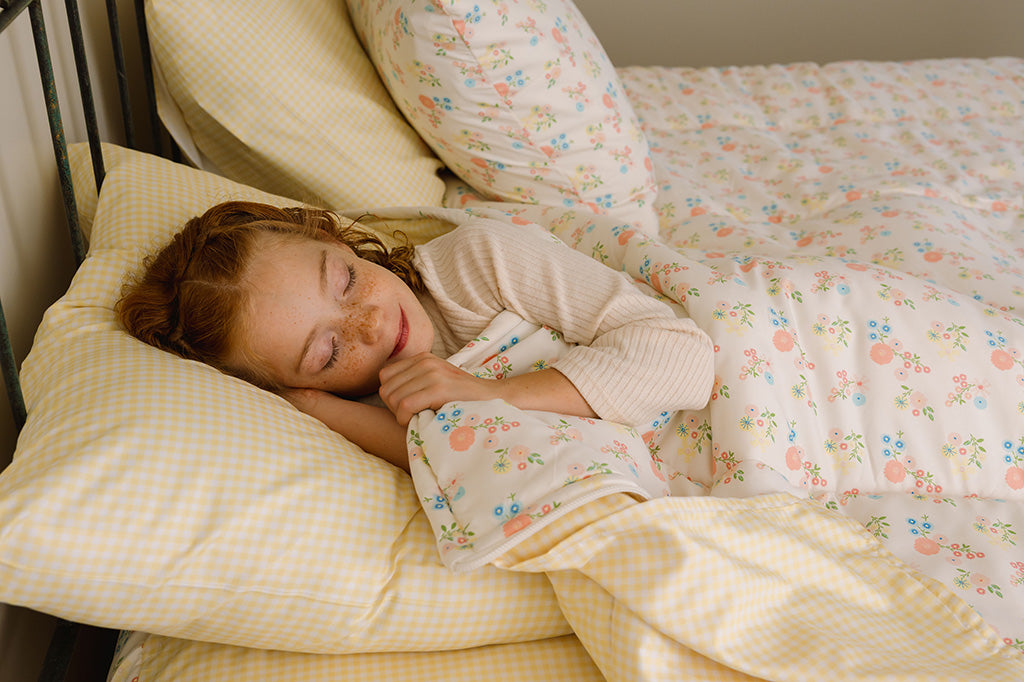 A young girl sleeping in yellow gingham and floral bedding.