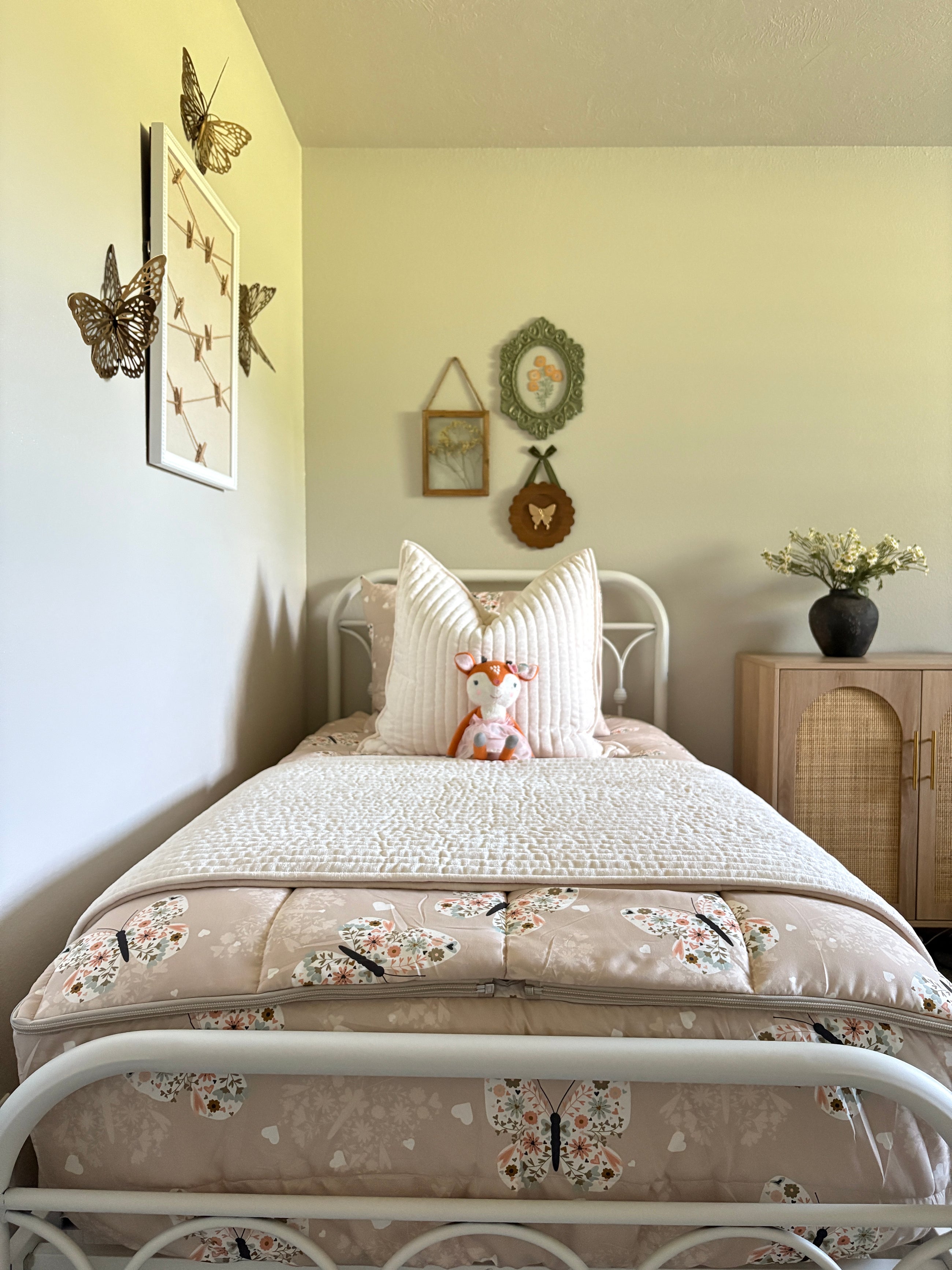A girls room featuring a white iron bed made with butterfly zipper bedding, a stuffed fox propped against the pillows.