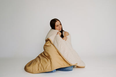 Girls cuddling in a yellow and cream blanket on a white background.
